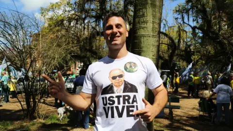 A man wears a T-Shirt with a picture of Carlos Alberto Brilhante Ustra