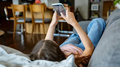 Getty Images Teenage girl at home looking at social media on her cell phone while lying on the couch