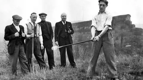 Four older men watch as a younger man hits a ball in Knurr and Spell in October 1953. Alamy: single-use only.