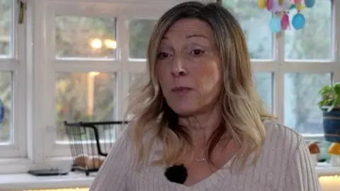 Shaun Whitmore/BBC Sue Farthing is sitting and looking to the left of the camera. She is wearing a cream coloured jumper and has her hair down.