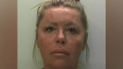 Devon and Cornwall Police The image shows a single, tightly cropped head-and-shoulders custody-style photograph against a plain light background. The person faces the camera directly with hair tied up and is wearing a light-coloured top, with no visible objects or text in the frame.