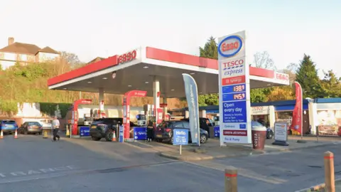 Google An Esso-branded petrol station, a row of houses and trees sits behind the station.