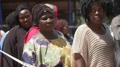 A queue of women standing in the sun, waiting to vote.