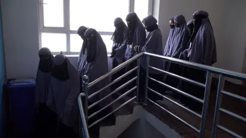 Women, with their faces covered, walk some stairs at the school