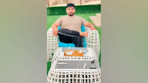 Tiktok/Fadi Gujjar Image shows Fadi Gujjar in Beachside Café. He wears a dark intermittent suit and a shirt and sits on a white chair. In the foreground, the schedule was set for dinner.