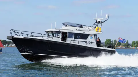 Dorset Police A large black and white boat travel through the water near a coastline.