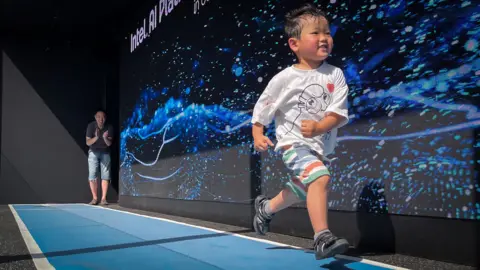 A little boy sprints down a track while his father watches