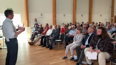 Miller speaks to the seated audience in the hall.