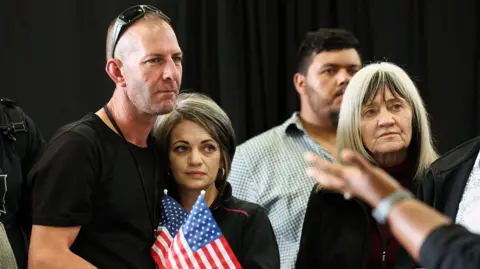 A man and a woman hugging holding American flags with stern expressions