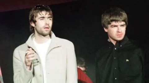 PA Media Oasis lead singer Liam Gallagher (left) and his brother Noel at the Cardiff International Arena in 1997