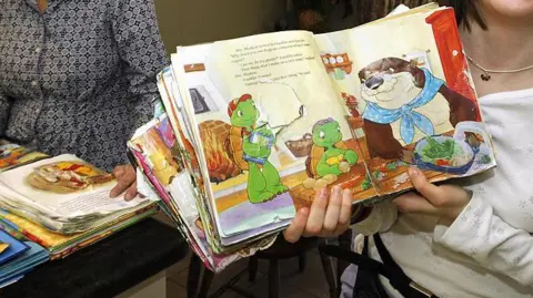 Toronto Star via Getty Images A child is smiling holding a Franklin the Turtle book open to a page showing Franklin 
