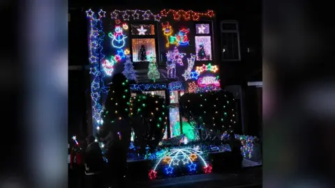 It is dark outside and a house is decked top-to-bottom in Christmas lights of all different colours. There are shooting stars, santas, reindeers, snowmen and all sorts of string lights.
