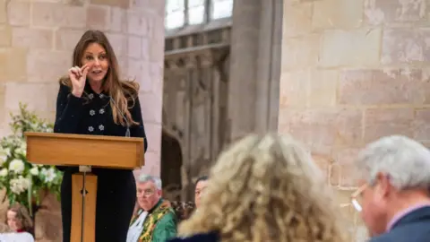Pictoria Carol Vorderman standing behind a lectern as she addresses the audience at Gloucestershire Cathedral.