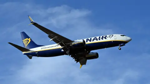 A Ryanair plane, seen here at Edinburgh Airport, flying against a background of a blue sky