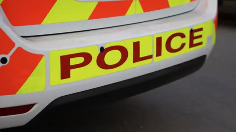 The rear bumper of a police car with POLICE written in red print on illuminous yellow background.