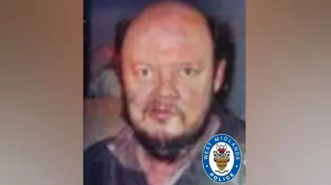 West Midlands Police A bald man with some brown hair on the sides of his head and a beard wearing a black shirt.