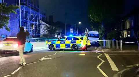 A police cordon and a blue and yellow police car seen 