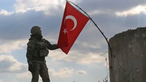 Turkish soldier with national flag on a mountain on the Syrian-Turkish border, north of Azaz on January 28, 2018