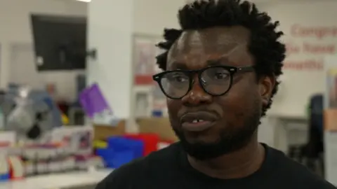 Close shot of Diawuoh, who is looking past the camera, wearing glasses and a black t-shirt.