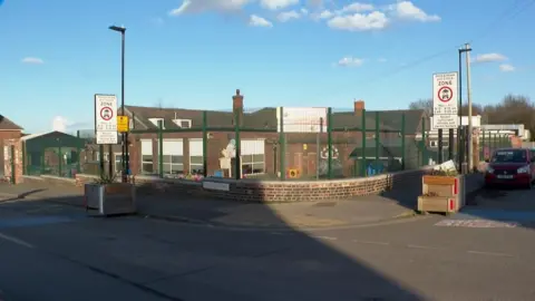 A red-brick building with a concrete front yard and signs warning of parking restrictions.