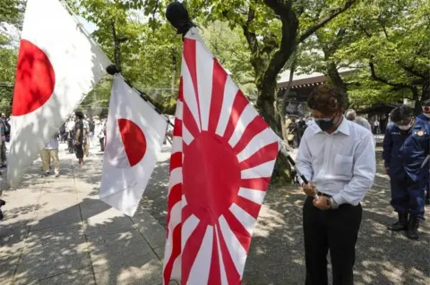 EPA People holding Japan"s national flags and the rising sun flag offer one minute silence for the war dead at Yasukuni Shrine