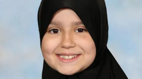 SURREY POLICE a young girl is pictured smiling at the camera. She is wearing a black hijab