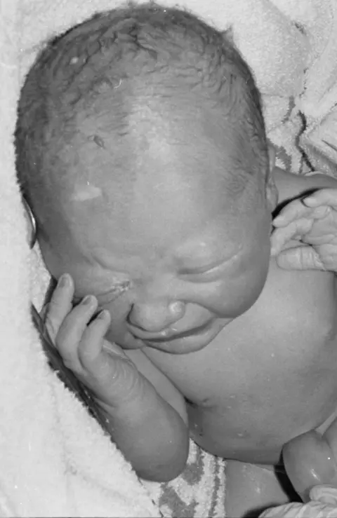 Francis Sanders Ester moments after she has been born. The black and white photograph shows her lying down with one hand held to her face. She is crying.