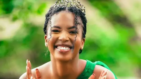 Lesego Chombo in a diamond tiara smiles - she's wearing a green dress with a single strap against a green background