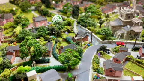 A close up image of the Gnosall model village which includes the church, houses, cars, gardens and people.