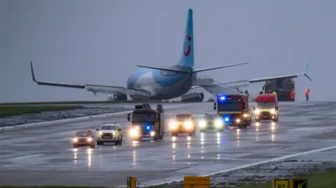 PA Media Emergency services on the runway at Leeds Bradford Airport with a TUI jet on the grass verge 