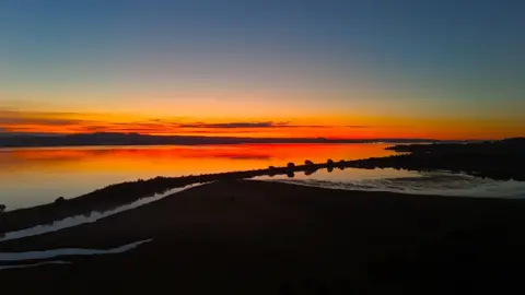 Kevin Hamill Landscape panoramic of a loch at sunrise with a burnt orange sky reflected in the water