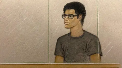 Julia Quenzler/BBC Court sketch of Nicholas Prosper appearing in the dock at Luton Crown Court, Bedfordshire. He has a dark top and black rimmed glasses.