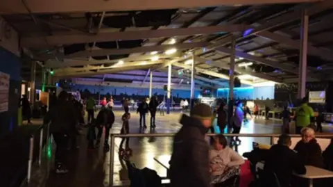 Interior shot of Skateland, showing a large internal area with people roller skating while others sit at table around the outside
