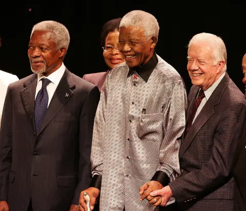 Getty Images Nelson Mandela (C), duke festuar ditëlindjen e tij të 89-të, qëndron i rrethuar nga ish-presidenti i SHBA-së Jimmy Carter (R) dhe ish-shefi i OKB-së Kofi Annan (L), gjatë ceremonisë së nisjes së grupit të njohur si The Elders 18 korrik 2007 në Johannesburg.