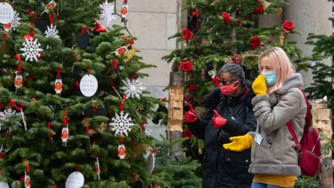 PA Media Women in face masks looking at Christmas trees