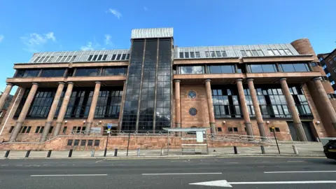 An imposing court made made from red stone, columns and large dark windows.