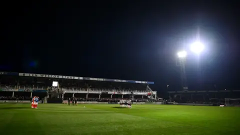 Getty Images A grassy pitch with football stands and a floodlight in the distance, seen at night