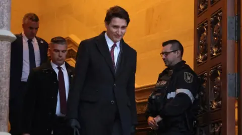 Prime Minister Justin Trudeau leaves Parliament Hill after a cabinet meeting in Ottawa, wearing a dark coat over a suit and tie. He is flanked by security staff