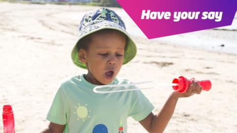 Boy blowing bubbles in sun hat.