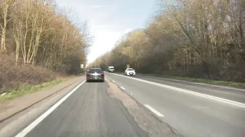 A road where a large section of tarmac has come away from the centre of the carriageway revealing concrete beneath