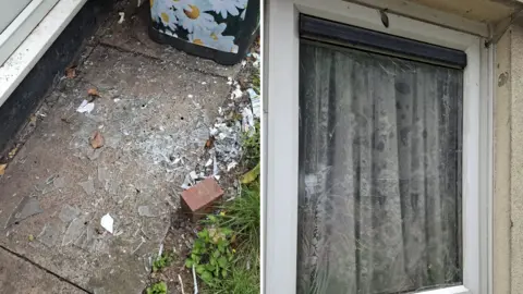 Charlie Williams Composite image showing a damaged residential window. On the left, broken glass shards are scattered across a concrete path beside a house wall, with a planter and small brick nearby. On the right, a close-up of the window shows cracked and shattered glass still in the frame, with curtains visible behind the pane. The image documents apparent window damage and resulting debris.