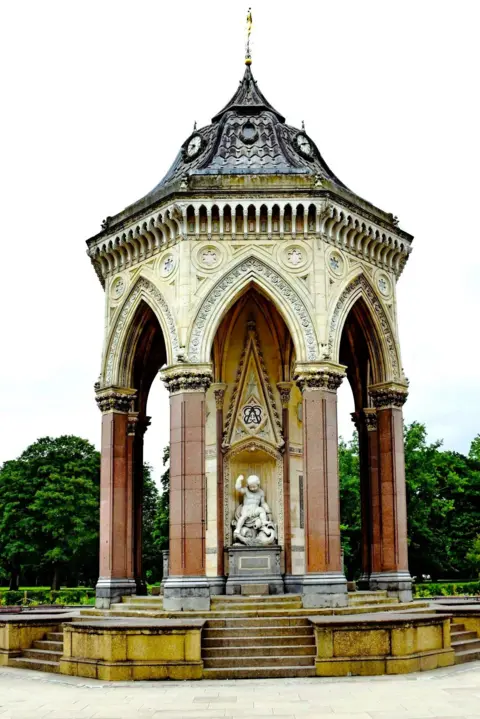 Historic England A sculpted water fountain made up of columns and stairs leading up to a statue of a small child 