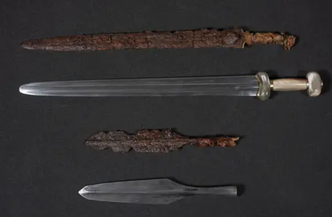National Museums Scotland / PA An Iron Age spearhead and sword, both heavily rusted with age. Modern replicas are displayed beside them