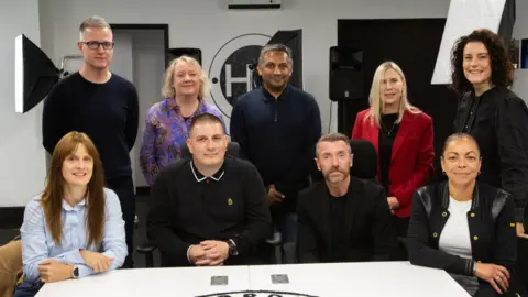 The Leicester Music Board pose for a group photo. There are nine people, four are sat down with five stood in a row behind them.