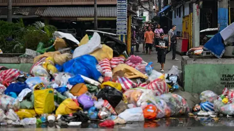 A pile of multi-coloured rubbish on a street. There are people walking behind it.