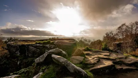 Jenni Shepherd/National Trust A sunset over rock formations with moors in the distance