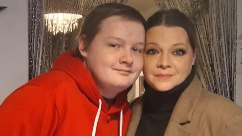 Jolanta Otlewska A teenage boy who is quite tall but young in the face. He has short brown hair and is leaning down slightly to hold his face next to his mum's. She has brown hair in a smooth ponytail. Both smile at the camera.