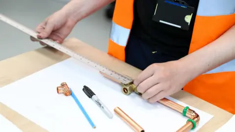 Northampton College Person using a ruler to measure some metal piping on a wooden desk