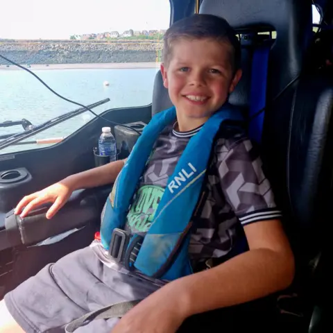 Barry Dock RNLI Marley sits in a leather chair in a boat. He wears a blue life jacket and smiles at the camera. 