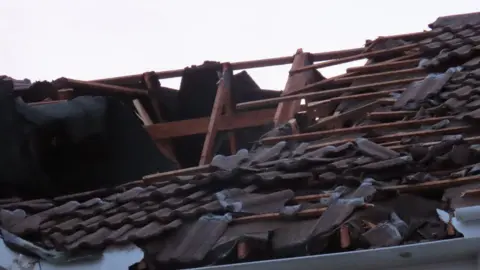 BBC A picture of a damaged roof. There is a number of panels missing, with wooden structure showing.
